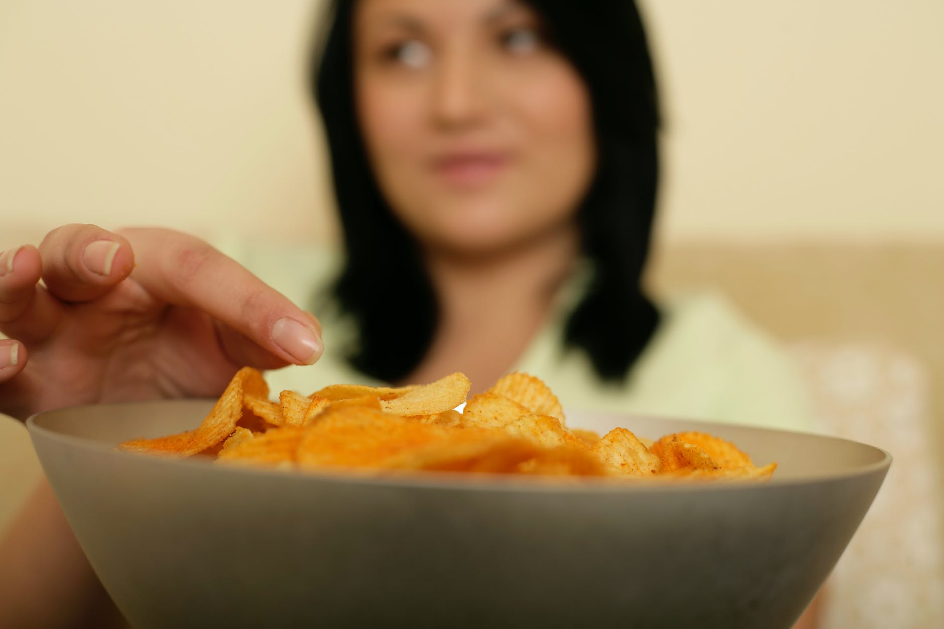 photo of a bowl with crisps and a woman in the background reaching for the crisps